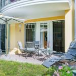 Terrasse mit Sitzgruppe, Sonnenschirm und Liegestühlen vor gelbem Haus.