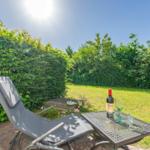 Außenterrasse mit Liegestuhl und Tisch mit Weinflasche und Gläsern. Grünhedge und Rasen im Hintergrund.