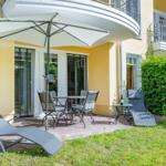 Terrasse mit Sonnenschirm, Tisch, Stühlen und Liegestühlen vor gelbem Haus