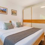 Schlafzimmer mit Doppelbett, Holzmöbel und Garderobe. Wandbilder und Nachttisch mit Lampe.