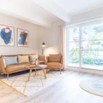 Wohnzimmer mit braunem Sofa, Sessel, Tisch und Fenster. Wandbilder und Teppiche sind sichtbar.