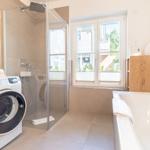 Badezimmer mit Dusche, Badewanne und Waschmaschine. Fenster mit Blick nach draußen.