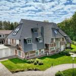 Haus mit grauem Dach, Ziegelfassade und gepflegtem Garten unter blauem Himmel.