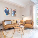Ein Wohnzimmer mit braunem Sofa, Sessel und Holztisch. An der Wand hängen zwei abstrakte Bilder.