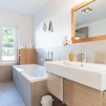 Badezimmer mit Badewanne, Waschbecken und Fenster mit Blick nach außen.