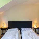 Zwei Betten mit weißen Bettwäsche, schwarze Nachttische mit Lampen, schräges Dach und Wandbild.