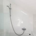 Dusche mit Duschbrause und Handbrause in Badewanne mit Glaswand und Handtuchhalter.