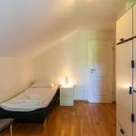 Schlafzimmer mit Einzelbett, Nachttisch und Kleiderschrank. Holzboden und schräges Dach.