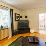 Wohnzimmer mit Holzboden, Sofa, Fernseher und Fenster mit Blick auf Wald.