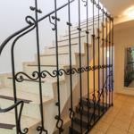 Treppe mit schmiedeeisernem Geländer und hellen Stufen führt zum Obergeschoss.