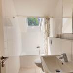 Badezimmer mit Dusche, Waschbecken und Fenster. Weiße Fliesen und Spiegel.