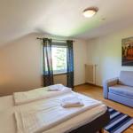 Zimmer mit Bett, Sofa und Fenster mit Blick. Wandbild zeigt Stadtansicht.