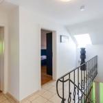 Flur mit Treppe, Tür zu Schlafzimmer und Wohnzimmer. Dachfenster und schwarze Pflanze.