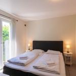 Schlafzimmer mit Doppelbett, zwei Nachttischen und Glastür zum Garten.