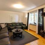 Wohnzimmer mit L-förmigem Sofa, zwei runden Tischen und Fenster mit Blick ins Grüne.