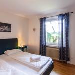 Schlafzimmer mit Doppelbett, Fenster und Gardinen.