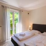 Schlafzimmer mit Bett, Nachttisch und Fenster zur grünen Außenseite.