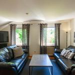 Wohnzimmer mit zwei Ledersofas, Fernseher und Fenstern mit Vorhängen.