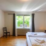 Schlafzimmer mit Bett, Kleiderschrank, Stuhl und Fenster mit Blick auf Grün.