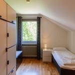 Schlafzimmer mit Einzelbett, Kleiderschrank und Fenster mit Blick auf Bäume.