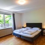 Schlafzimmer mit Doppelbett, Fenster mit Blick auf Grün, Holzboden und zwei Nachttische.