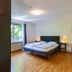 Schlafzimmer mit Doppelbett, Holzboden und Fenster mit Blick auf Grün.