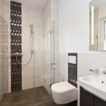 Duschbereich mit Glaswand, Toilette und Waschbecken mit Spiegel.