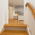 Treppenhaus mit Holzstufen und weißer Balustrade führt in ein Schlafzimmer mit Bett und Kleiderschrank.