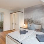 Schlafzimmer mit Dachschrägen, Bett, Kleiderschrank und Blick in die Dusche.