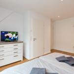 Schlafzimmer mit Bett, TV und Schrank. Holzboden und weiße Wände.