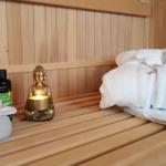 Sauna mit Holzbank, gefaltetem Handtuch, Duftölen und brennender Buddha-Lampe.