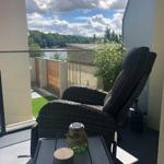 Terrasse mit Liegestuhl und Tisch. Blick auf Wasser und Bäume.