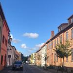 Enge Straße mit historischen Gebäuden und gepflastertem Boden unter blauem Himmel.