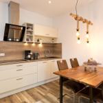 Küche mit Essbereich, Holztisch, Stühle und Holzoptik an der Wand.