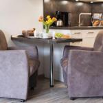 Zwei graue Sessel stehen an einem Tisch mit Frühstück und Blumen. Hintergrund ist Küche mit Arbeitsplatte.