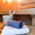 Sauna mit Holzbank, gefalteter blauer Handtuch und weißem Badetuch, daneben Eimer mit Holzlöffel.