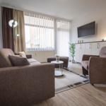 Wohnzimmer mit Sofa, Sessel, Fernseher und Fenster mit Jalousien.