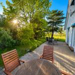 Terrasse mit Holztisch und Stühlen, Blick auf grüne Bäume und einen sonnigen Himmel.