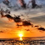 Sonnenuntergang über dem Wasser mit orangefarbenem Himmel und dunklen Wolken.