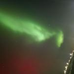 Grün leuchtende Nordlichter über einem beleuchteten Weg bei Nacht.