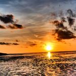 Sonnenuntergang über Wasser mit Wolken und Reflexion.