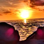 Sonnenuntergang über dem Wasser mit Felsen im Vordergrund.