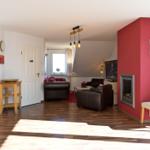 Wohnzimmer mit roter Wand, Kamin, Ledersofa und Holzboden. Küche im Hintergrund.