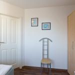 Schlafzimmer mit Bett, Kleiderschrank und Stuhl. An der Wand hängen zwei Bilder.