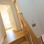 Holzgetreppe mit Handlauf führt zu einem Raum mit Holzboden und weißer Tür.
