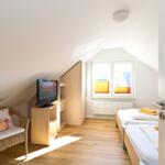 Zimmer mit zwei Betten, TV und Sitzgelegenheit unter Dachschräge.