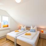 Zimmer mit zwei Betten, Fenster und Nachttisch.