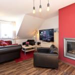 Wohnzimmer mit roter Wand, Kamin, Sofa und Fernseher.