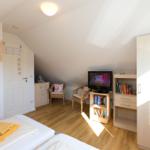 Schlafzimmer mit Dachschrägen, Bett, Fernseher und Schränken.