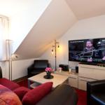 Wohnzimmer mit Sofa, Sessel und Fernseher unter Dachschräge